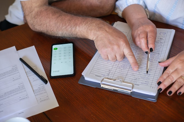 Two people at a table reviewing paperwork on a clipboard with a calculator and pen, discussing payment