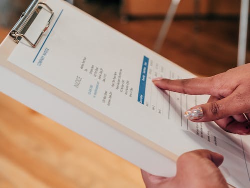 Person reviewing a printed proforma invoice template on a clipboard — showcasing key invoice details used for cost estimation and approval before final sale.