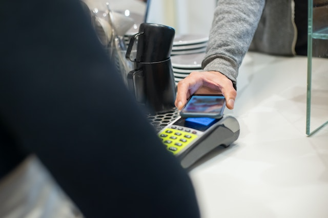 Customer tapping a smartphone on a card terminal to make a contactless payment at a counter