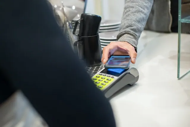 Customer tapping a smartphone on a card terminal to make a contactless payment at a counter