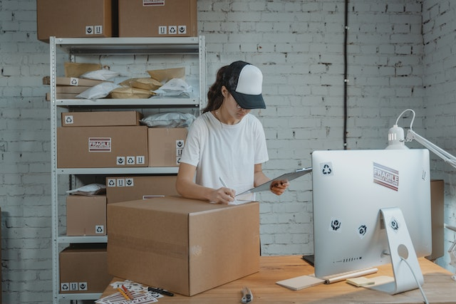 Warehouse worker reviewing a purchase order while preparing packages for shipment, showcasing inventory management and order fulfillment.