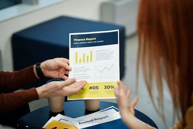 Two people reviewing a printed finance report with bar and line charts across a table