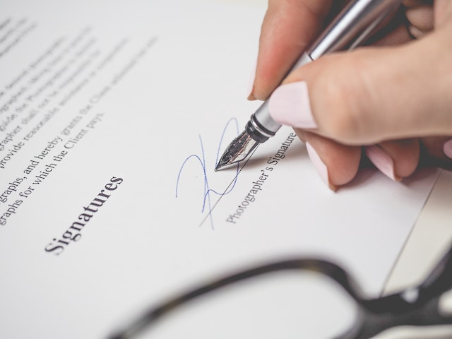 Close-up of a person signing a legally binding business document, emphasizing the formal agreement process tied to proforma invoices and client approvals before final transactions.