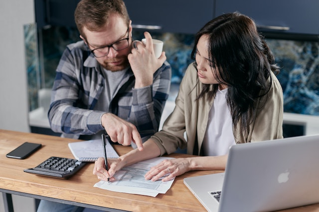 Two professionals reviewing a proforma invoice at a desk with a laptop, calculator, and documents – understanding the purpose and use of proforma invoices in business transactions.
